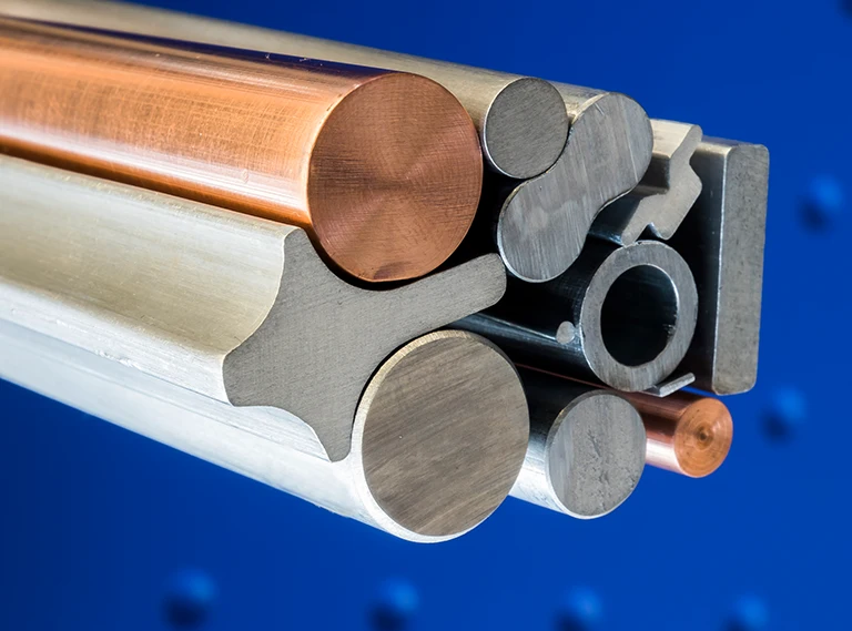 Mehrere Metallstangen und -stäbe mit unterschiedlichen Formen, Größen und Materialien, darunter runde, rechteckige und einzigartig geformte Profile, sind vor einem blauen Hintergrund aufeinander gestapelt.