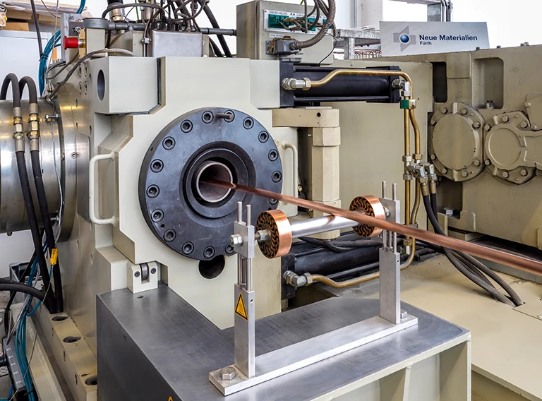 Ein Kupferdraht wird in einer großen industriellen Strangpressmaschine in einer Fabrikumgebung extrudiert, umgeben von Metallteilen, Rohren und Steuerelementen.