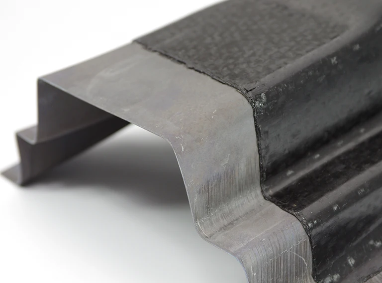 Nahaufnahme eines Teils aus Metall und Verbundwerkstoff mit einer gewellten, eckigen Form, die die Verbindung zwischen den beiden verschiedenen Materialien und ihre Texturen vor einem schlichten weißen Hintergrund zeigt.