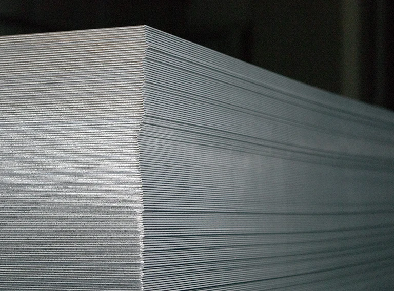 Eine Nahaufnahme eines großen, sauber gestapelten Stapels dünner, rechteckiger Metallbleche, die ihre glatten Kanten und die schichtweise Anordnung zeigen. Der Hintergrund ist dunkel und lenkt die Aufmerksamkeit auf die metallische Textur.