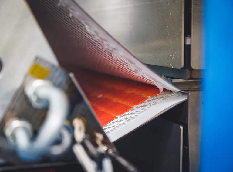 Nahaufnahme einer Maschine, die eine Materialplatte mit einem rot-weißen Gittermuster bearbeitet, das industrielle Metallkomponenten und mechanische Teile zeigt.