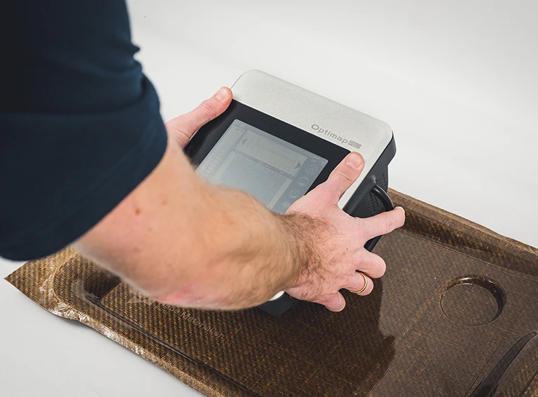 Eine Person arbeitet mit einem Ultraschallprüfgerät an einer braunen Kohlefaserverbundplatte und prüft deren Oberfläche auf Fehler.