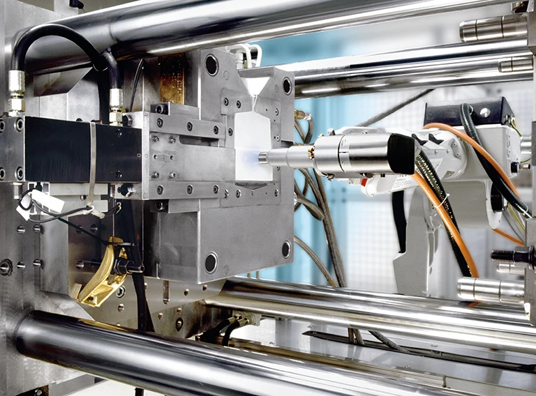 Nahaufnahme eines automatisierten Roboterarms, der eine industrielle Spritzgießmaschine bedient, mit Metallstäben und verschiedenen mechanischen Komponenten.