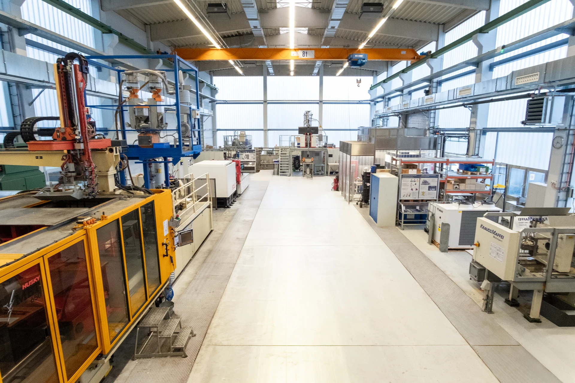 Eine geräumige, moderne Industriehalle mit verschiedenen großen Maschinen und Geräten auf beiden Seiten eines breiten Mittelgangs, mit heller Deckenbeleuchtung und großen Fenstern.