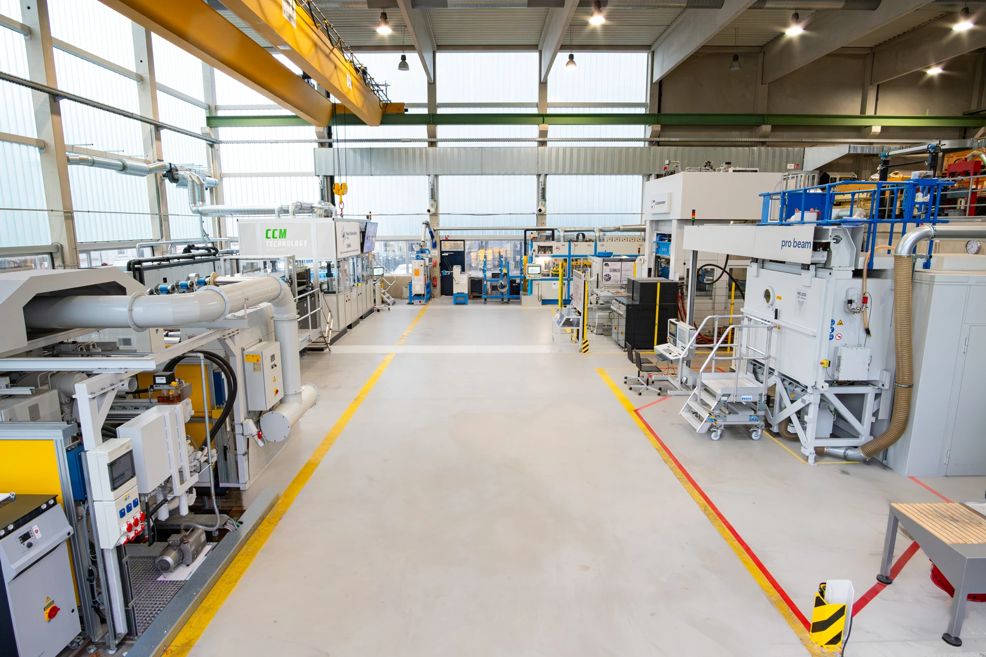 Eine saubere, gut beleuchtete Industriehalle mit verschiedenen modernen Maschinen und Geräten, breiten Gängen, hohen Decken, großen Fenstern und heller Deckenbeleuchtung. Es sind keine Menschen anwesend.