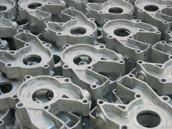 Eine Nahaufnahme vieler identischer Motorenteile aus Metall, die dicht nebeneinander gestapelt sind und kreisförmige Öffnungen und verschlungene Formen in einem sich wiederholenden, industriellen Muster aufweisen.